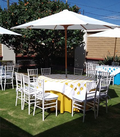 mesa-redonda-cubre-versalles-mantel-amarillo-sombrilla-y-sillas-tiffany-blancas